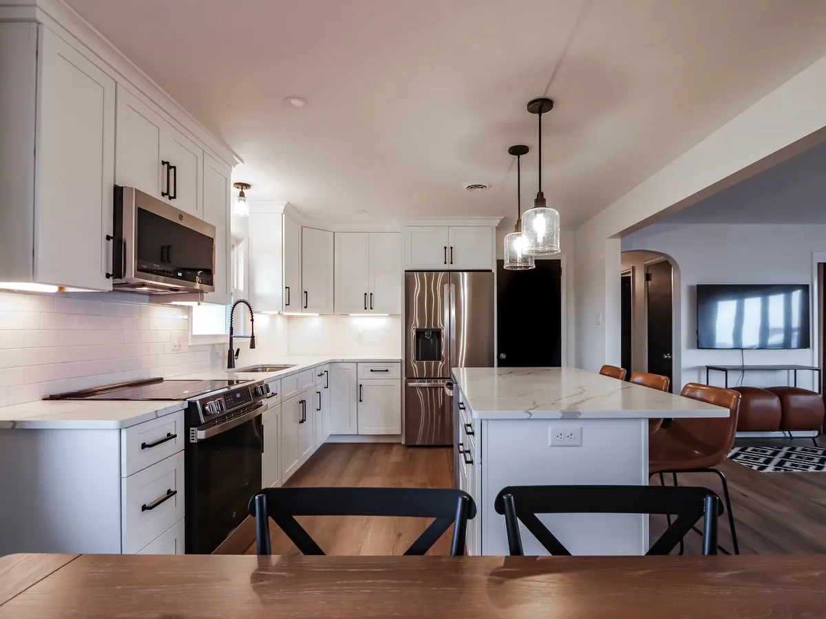 After: custom white kitchen with quartz island, pendant lights and hardwood floor