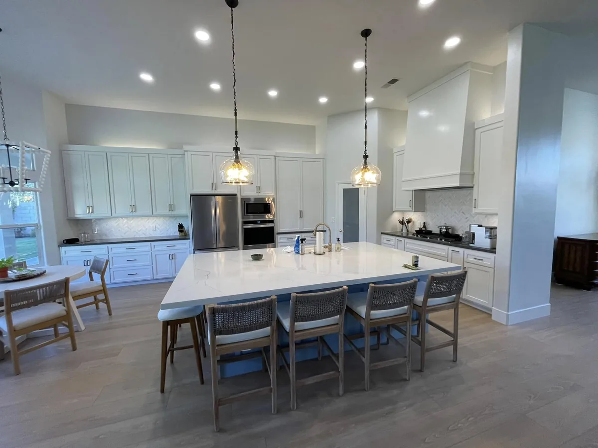 After: bright open-concept white kitchen with large quartz island and herringbone backsplash