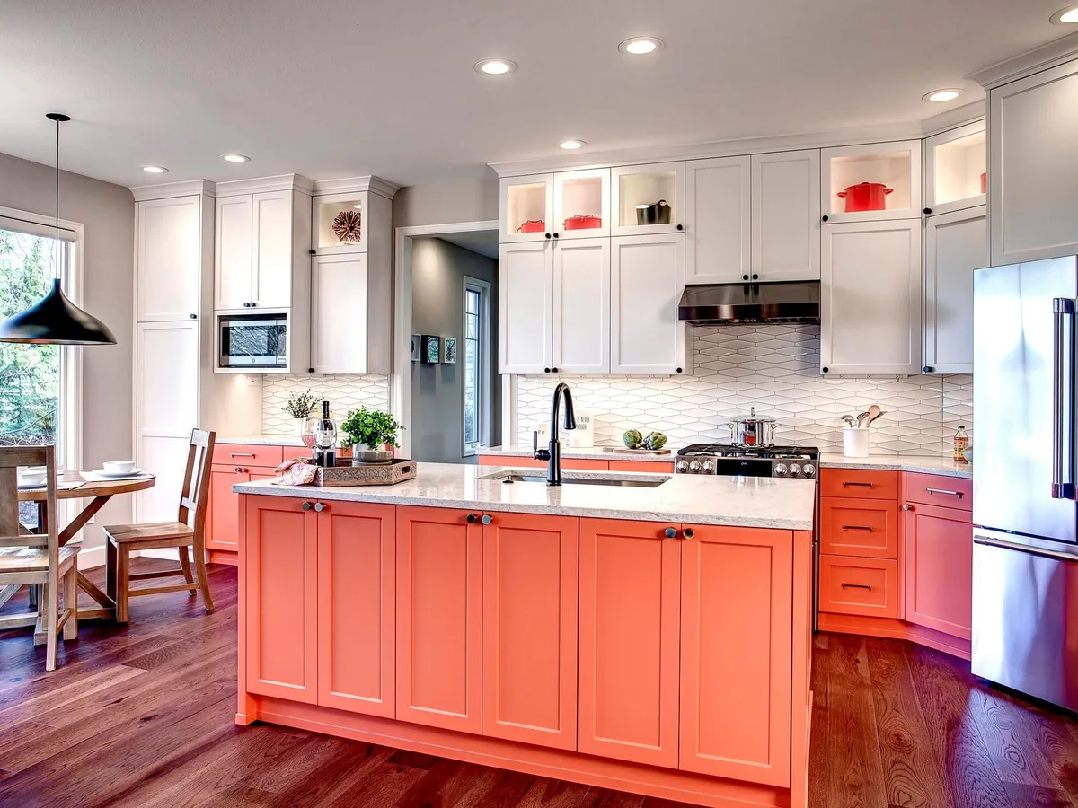 After: two-tone kitchen with white cabinets, a coral island and hardwood floor